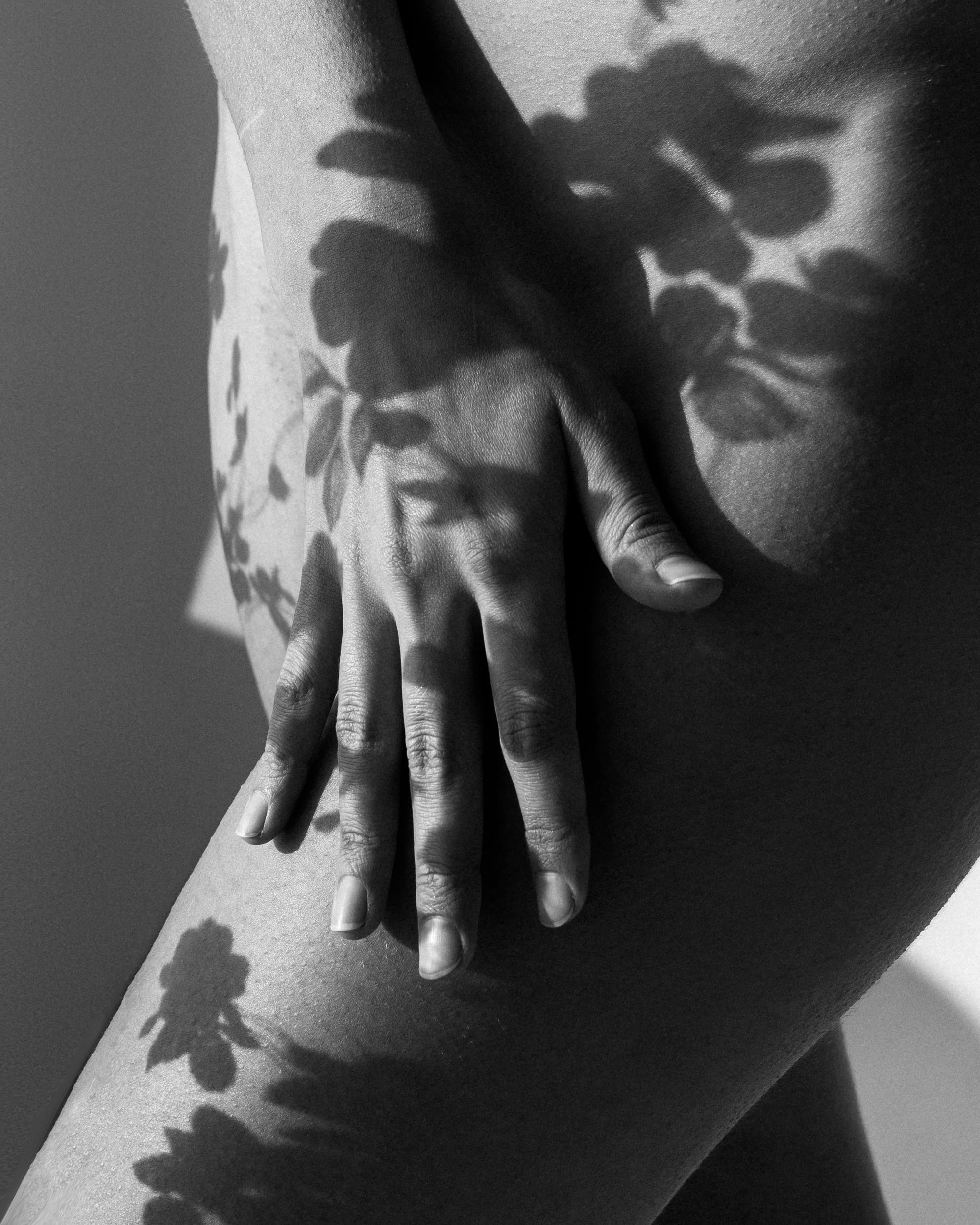 Black and white close-up of hands and floral shadows across a woman’s body