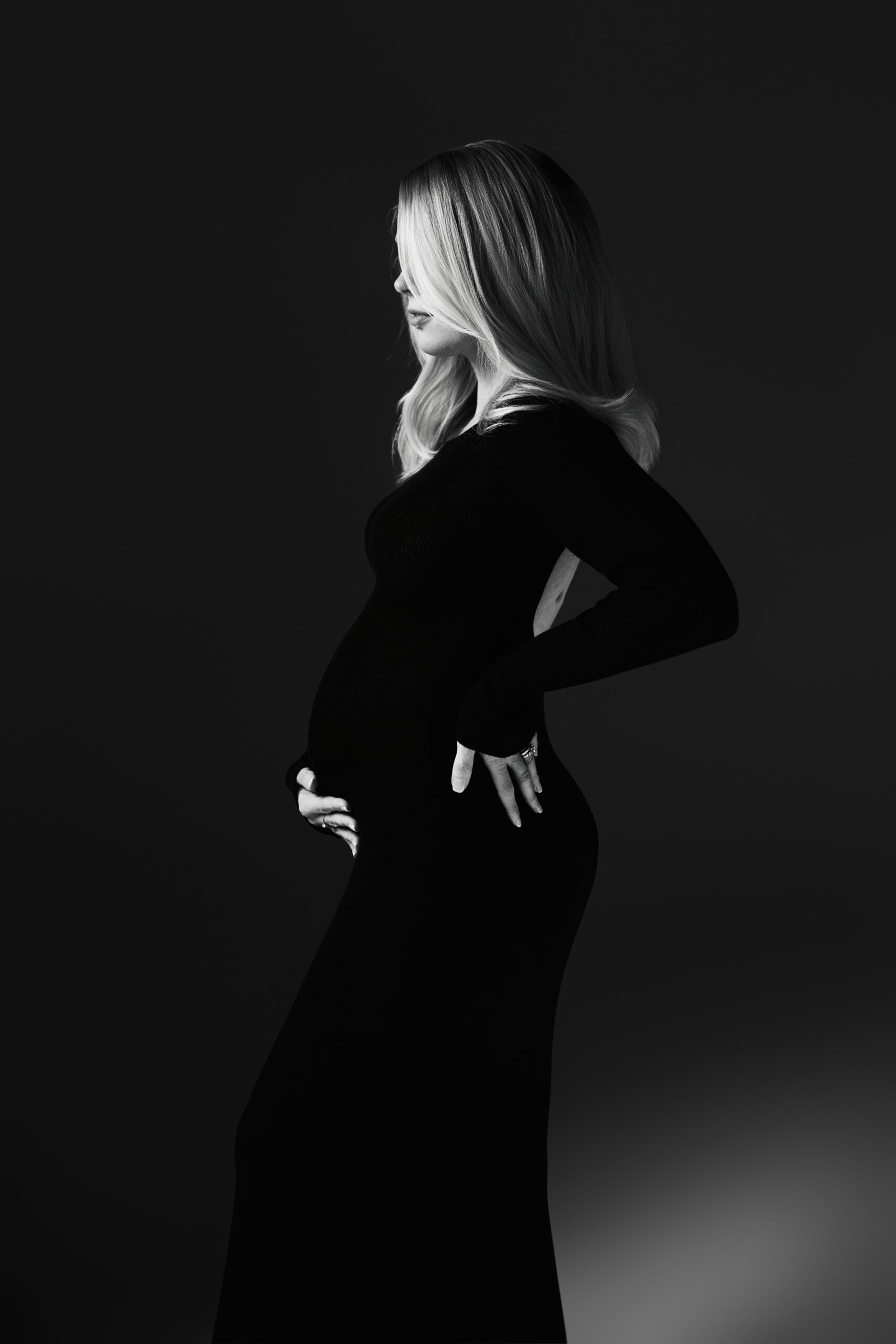 Pregnant woman in a fitted black dress seated on a studio stool