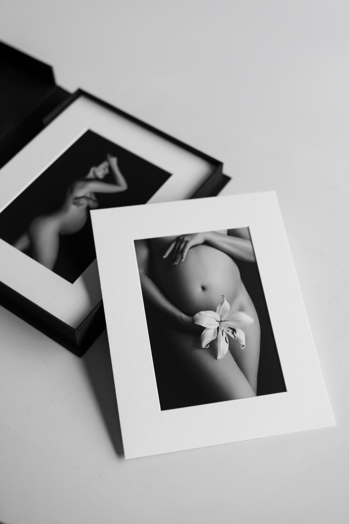Printed black-and-white maternity portraits with a white lily arranged in archival mats