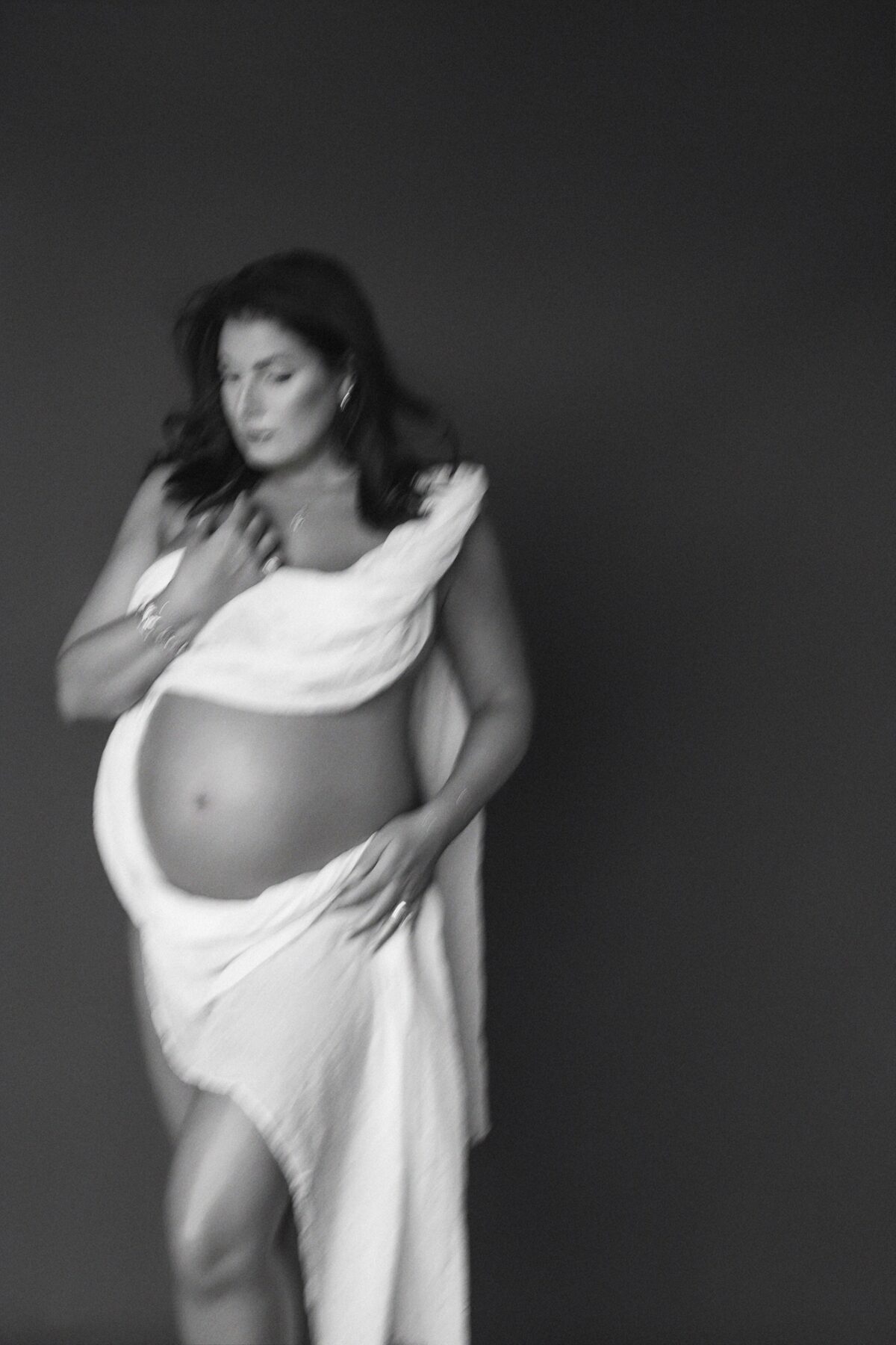 Pregnant woman draped in white fabric in an artistic motion-blur maternity portrait