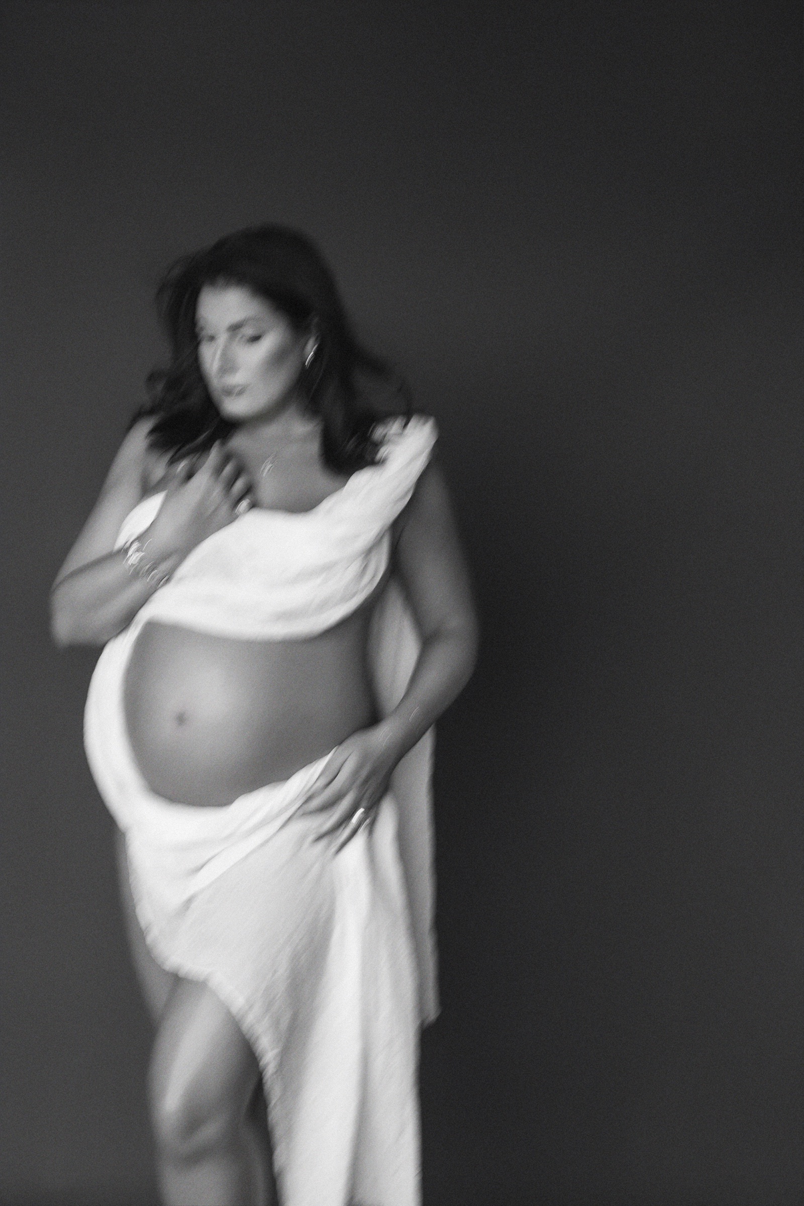 Pregnant woman draped in white fabric in an artistic motion-blur maternity portrait
