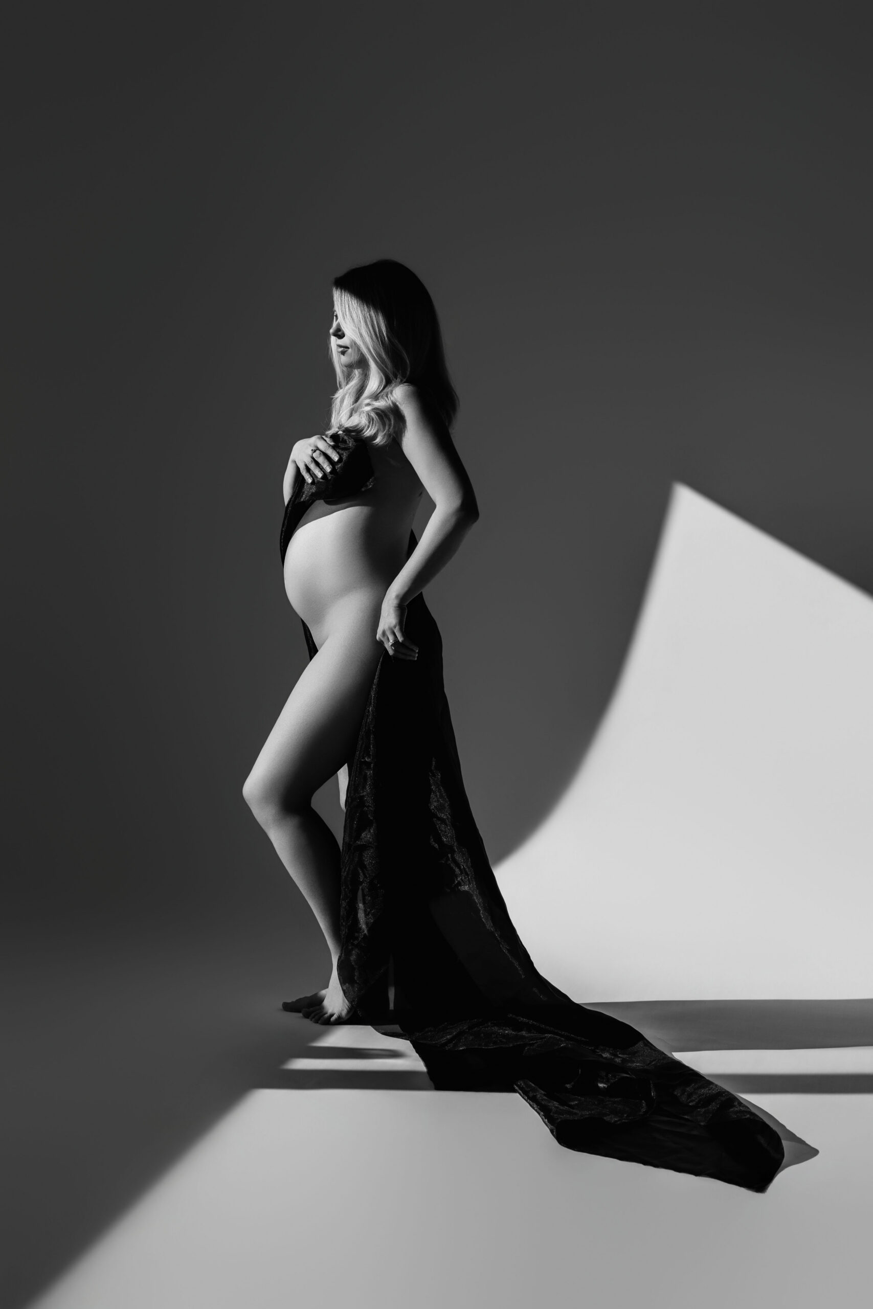 Pregnant woman in profile wearing a black lace drape in dramatic studio light