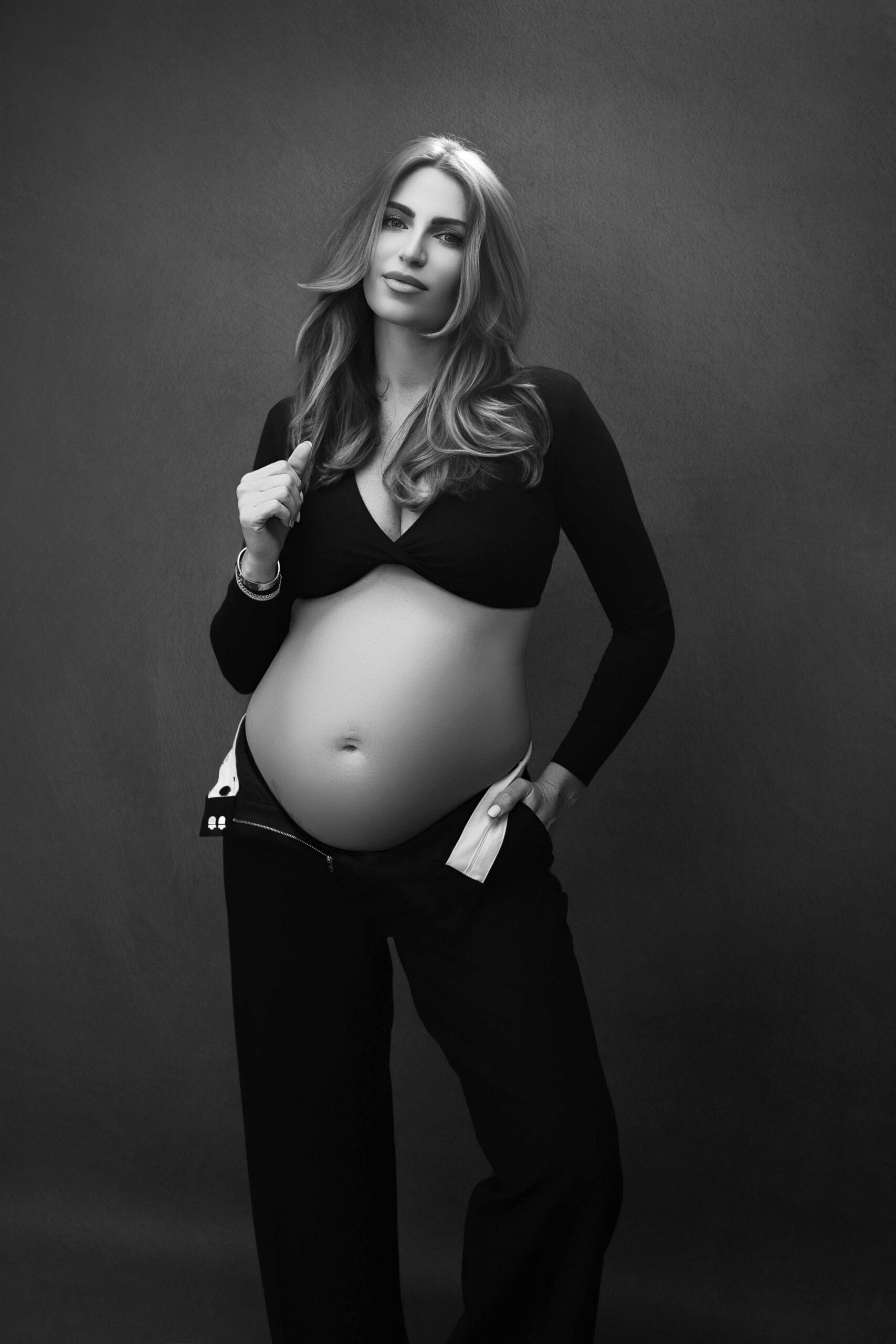 Pregnant woman wearing a black crop top and trousers against a textured studio backdrop