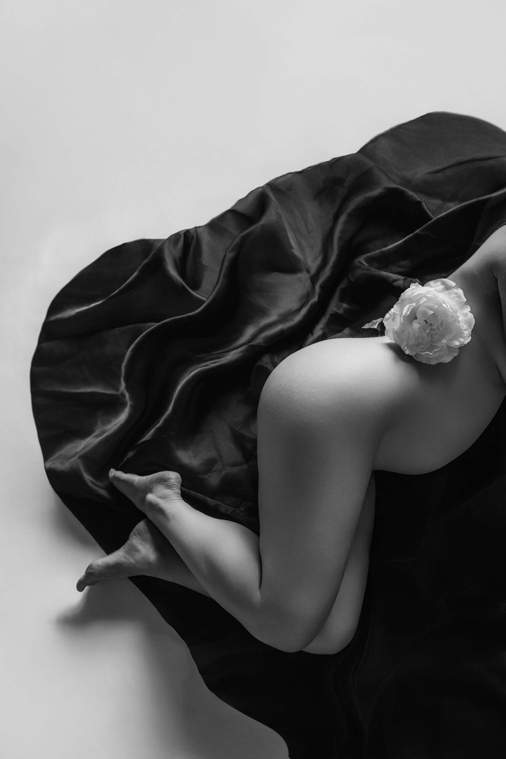 Pregnant woman reclining on dark fabric with a pale flower resting near her belly