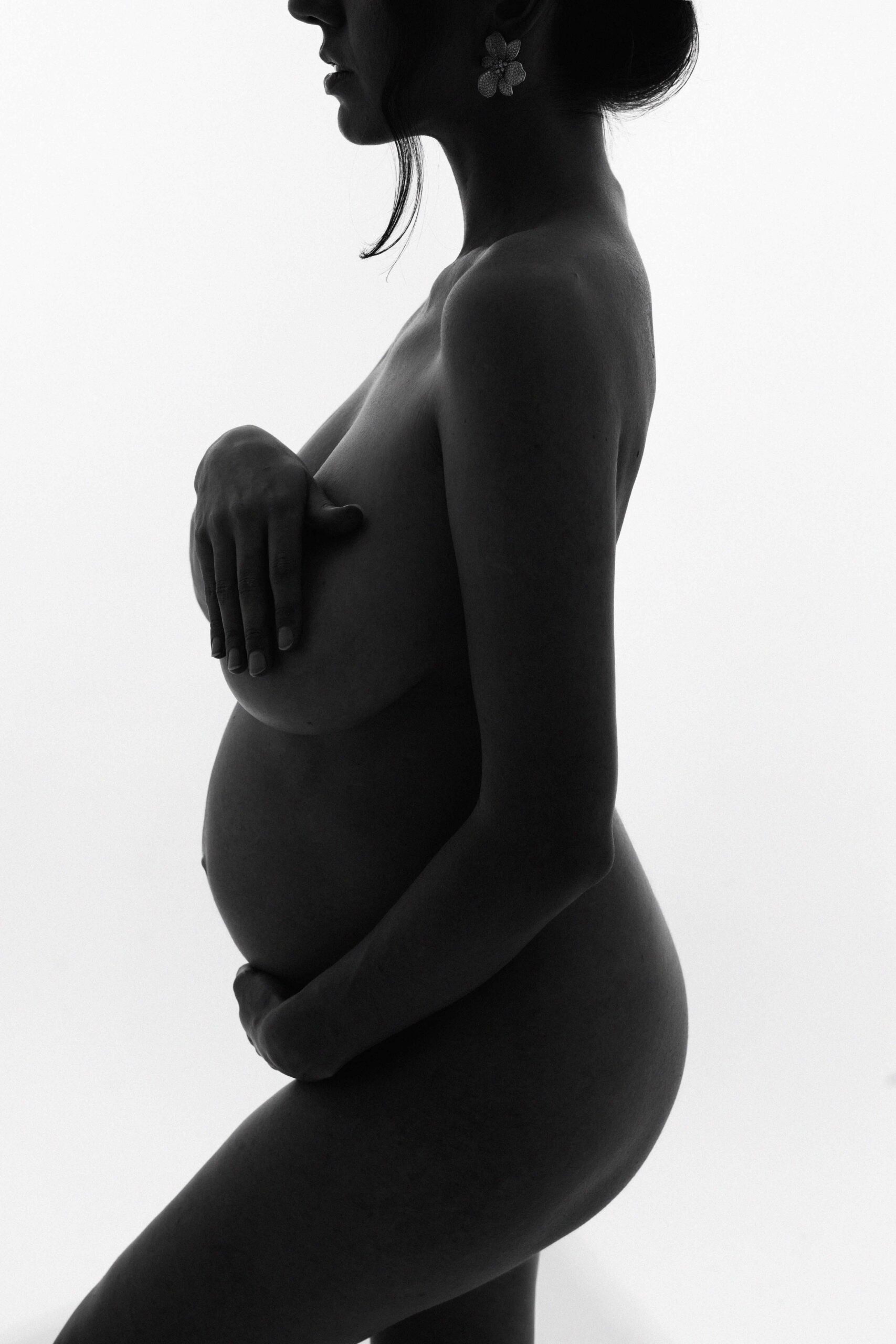 Pregnant woman in profile silhouetted against a bright studio background